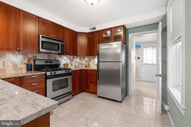836 N 25th St, Philadelphia, PA 19130 - kitchen with appliances with stainless steel finishes, tasteful backsplash, light stone counters, glass insert cabinets, and baseboards