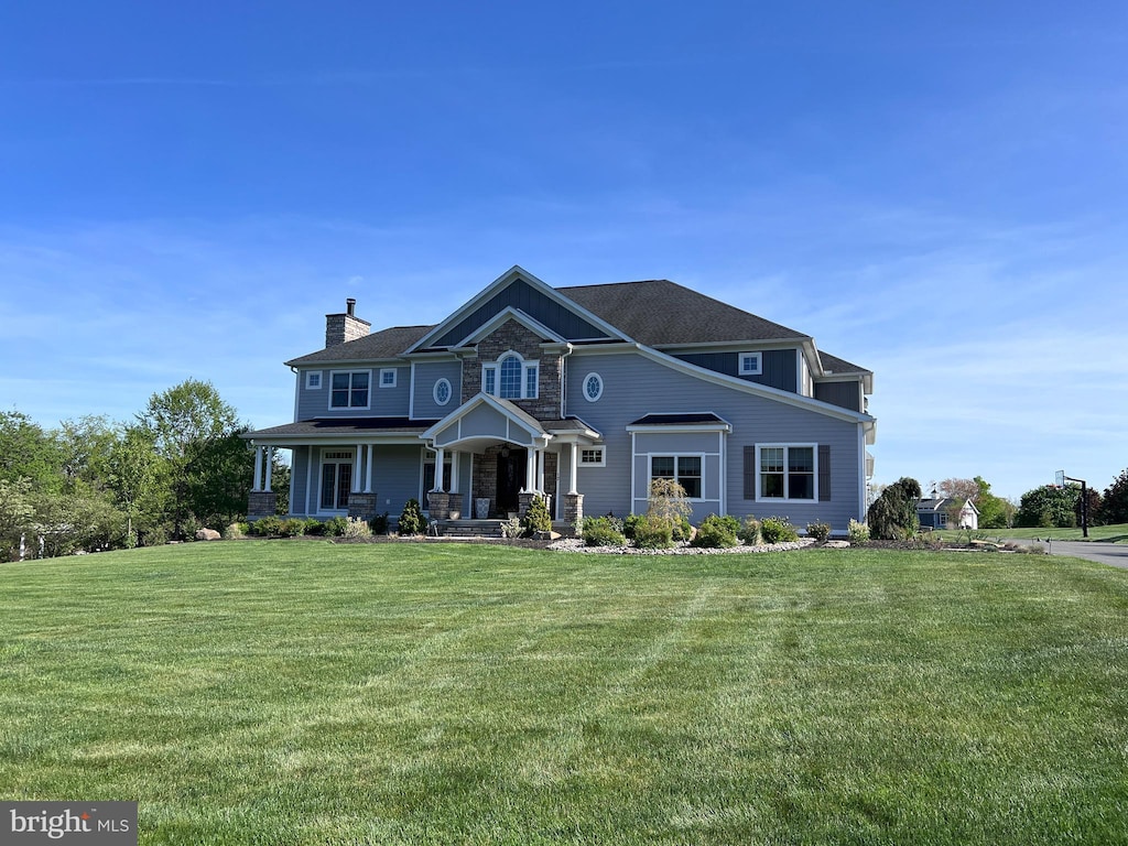 view of front facade with a porch, a chimney, a front yard, and stone siding