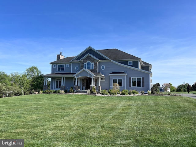 view of front facade with a porch, a chimney, a front yard, and stone siding