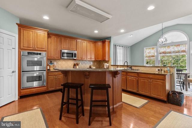 8 Warwick Ct, Newtown, PA 18940 - kitchen with stainless steel appliances, a breakfast bar, brown cabinets, a kitchen island, and vaulted ceiling