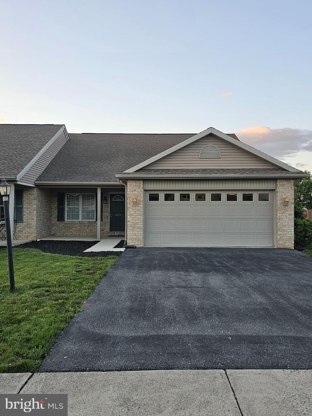 single story home featuring asphalt driveway, an attached garage, brick siding, and a front yard