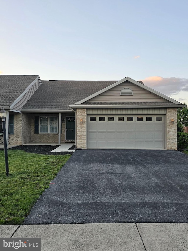 single story home featuring asphalt driveway, an attached garage, brick siding, and a front yard