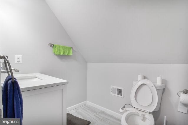 107 Main Ave SW, Glen Burnie, MD 21061 - half bath featuring vaulted ceiling, vanity, toilet, baseboards, and wood finished floors