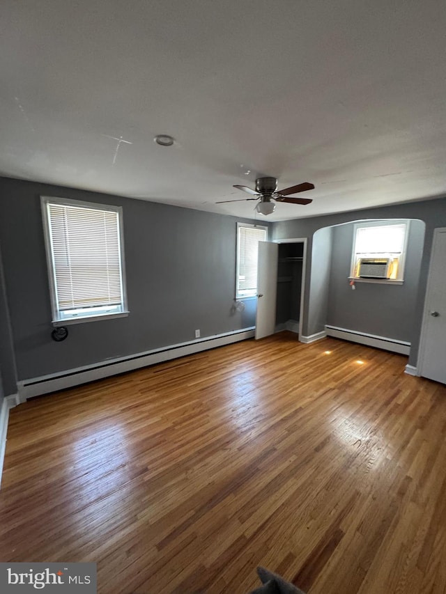 unfurnished bedroom with baseboard heating, multiple windows, and wood finished floors