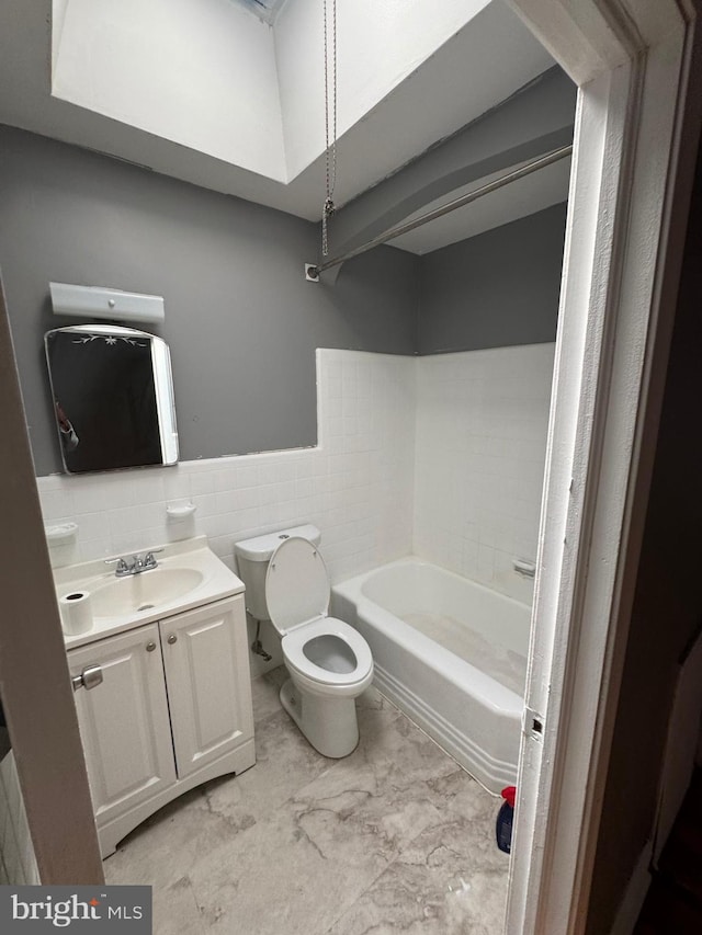 bathroom with a bath, vanity, marble look tile flooring, toilet, and tile walls