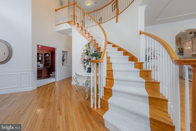 144 Cedar Ct, Woolwich Twp, NJ 08085 - stairway featuring a towering ceiling, arched walkways, hardwood / wood-style flooring, a wainscoted wall, and a decorative wall