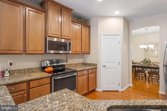 35206 Seagrass Plantation Ln, Dagsboro, DE 19939 - kitchen with stainless steel appliances, light wood-type flooring, a chandelier, light stone counters, and brown cabinetry