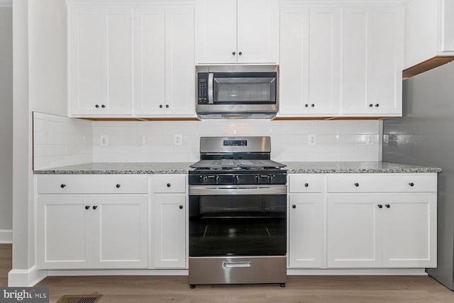 kitchen featuring stainless steel appliances, light wood finished floors, light stone counters, and white cabinets