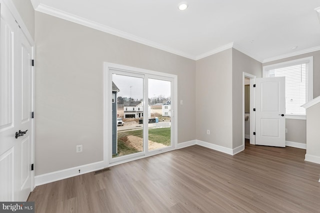 empty room featuring wood finished floors, baseboards, and crown molding