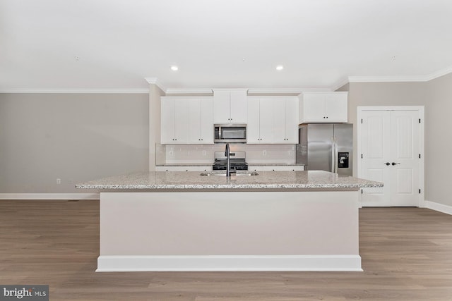 kitchen featuring appliances with stainless steel finishes, crown molding, a kitchen island with sink, baseboards, and white cabinets