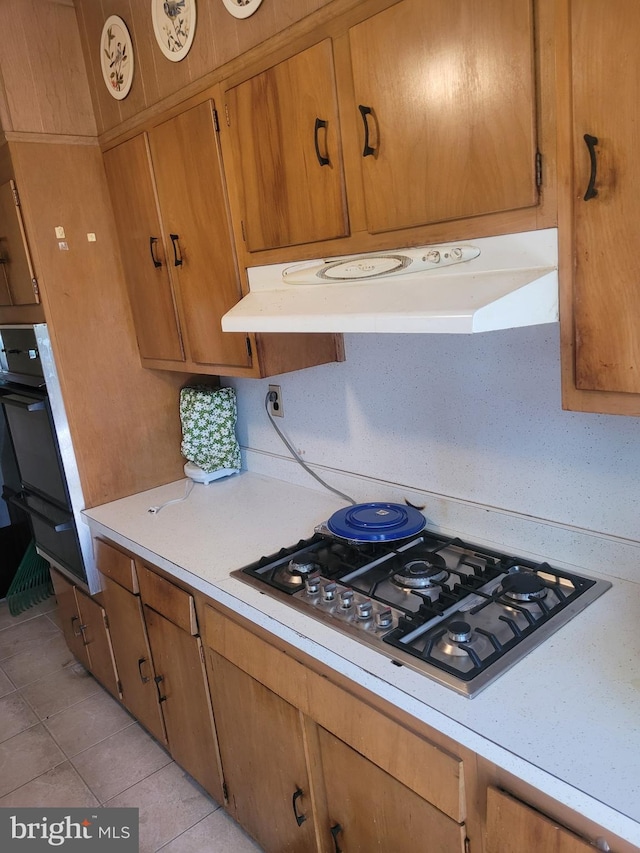 1605 Argonne Dr, Baltimore, MD 21218 - kitchen with under cabinet range hood, stainless steel gas stovetop, light countertops, light tile patterned floors, and brown cabinets