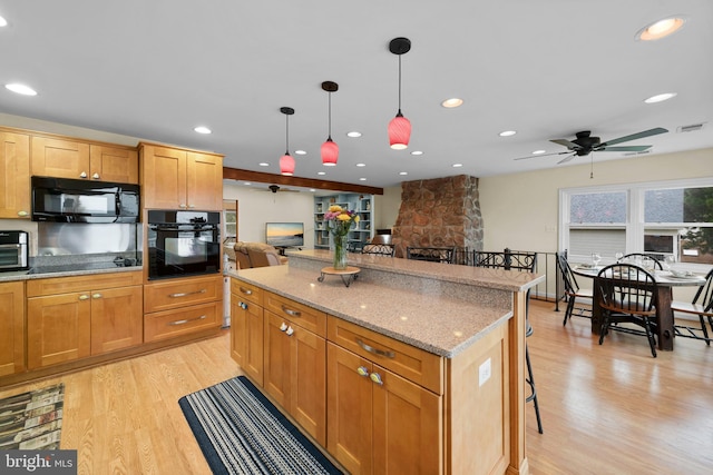 295 Chesapeake Ave, Prince Frederick, MD 20678 - kitchen with black appliances, light wood finished floors, a breakfast bar area, a fireplace, and hanging light fixtures