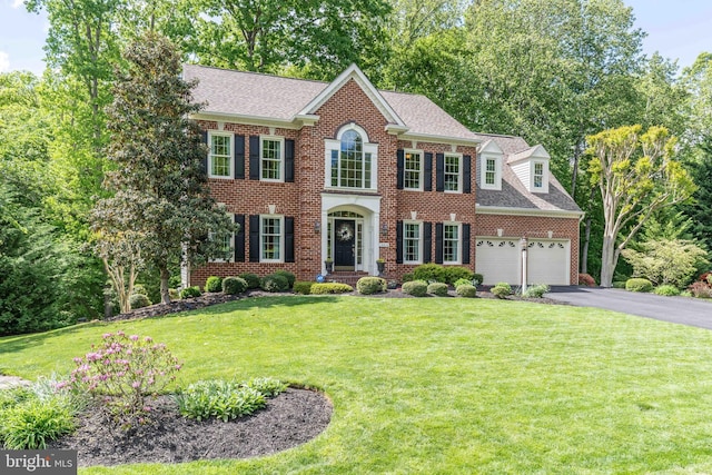 13016 Brookmead Dr, Manassas, VA 20112 - georgian-style home featuring driveway, brick siding, a front lawn, a shingled roof, and a garage