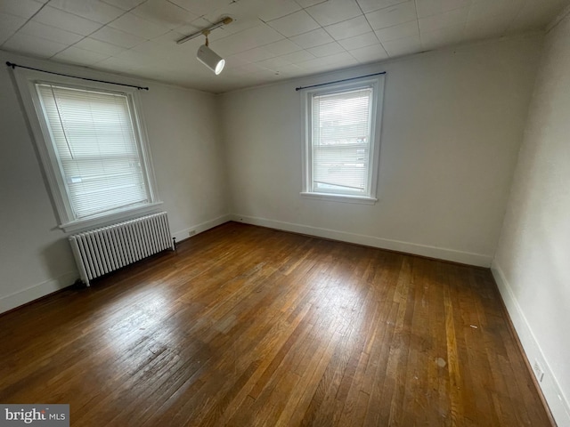 empty room with radiator, hardwood / wood-style floors, and baseboards