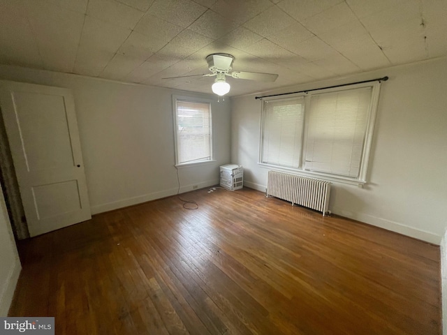 spare room featuring radiator, hardwood / wood-style flooring, a ceiling fan, and baseboards