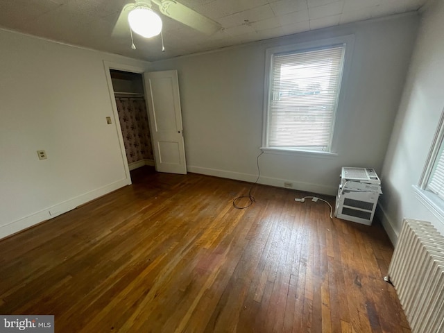 unfurnished bedroom featuring radiator heating unit, multiple windows, wood-type flooring, and baseboards