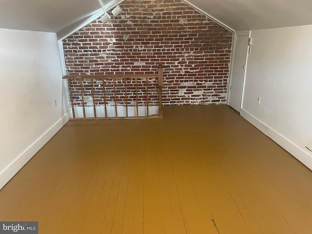 additional living space featuring brick wall, baseboards, and vaulted ceiling