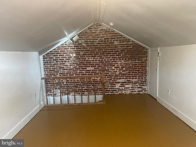 additional living space featuring brick wall, vaulted ceiling, baseboards, and wood finished floors