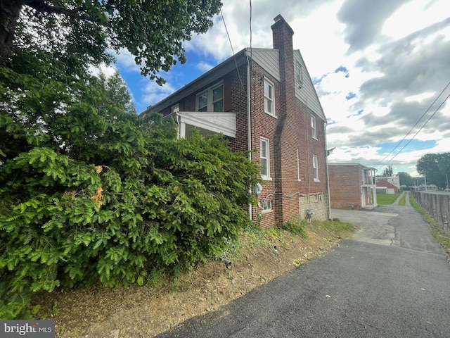 view of side of property featuring a chimney, brick siding, and driveway