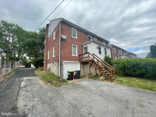 rear view of property featuring brick siding, a chimney, asphalt driveway, an attached garage, and stairway
