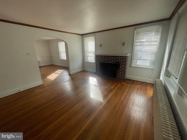 unfurnished living room with crown molding, arched walkways, baseboards, plenty of natural light, and wood finished floors