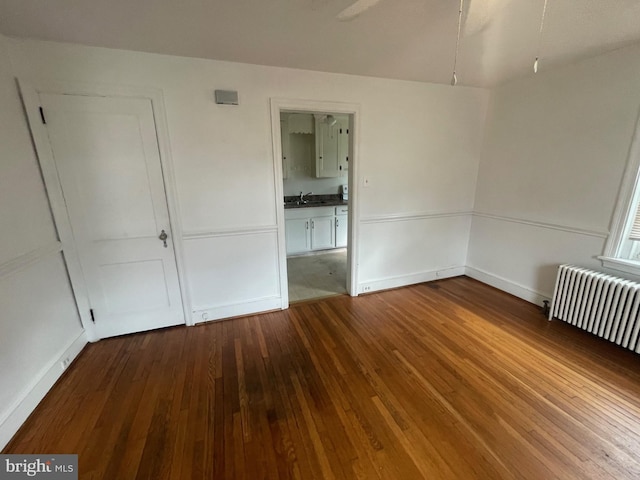 unfurnished bedroom featuring radiator, dark wood-style floors, a sink, and baseboards