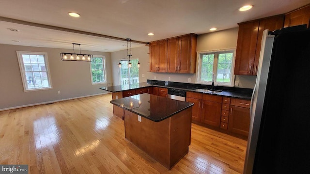 kitchen with dishwasher, a sink, a peninsula, freestanding refrigerator, and light wood-style floors