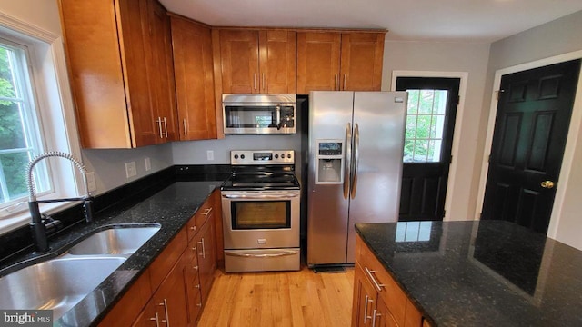 kitchen featuring stainless steel appliances, a sink, brown cabinets, light wood-style floors, and dark stone countertops