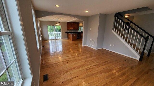 unfurnished living room with arched walkways, light wood-style floors, baseboards, stairway, and recessed lighting