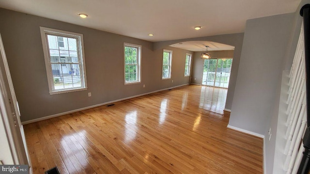 empty room featuring arched walkways, baseboards, light wood finished floors, and recessed lighting