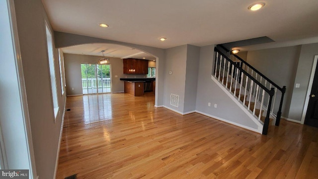unfurnished living room with arched walkways, light wood-type flooring, recessed lighting, baseboards, and stairway