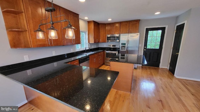 kitchen with appliances with stainless steel finishes, a sink, open shelves, brown cabinetry, and dark stone countertops