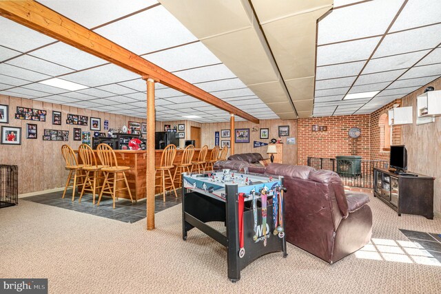 carpeted living area featuring a drop ceiling, wood walls, a dry bar, a brick fireplace, and baseboards