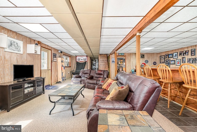 living room featuring wood walls, a paneled ceiling, and a bar