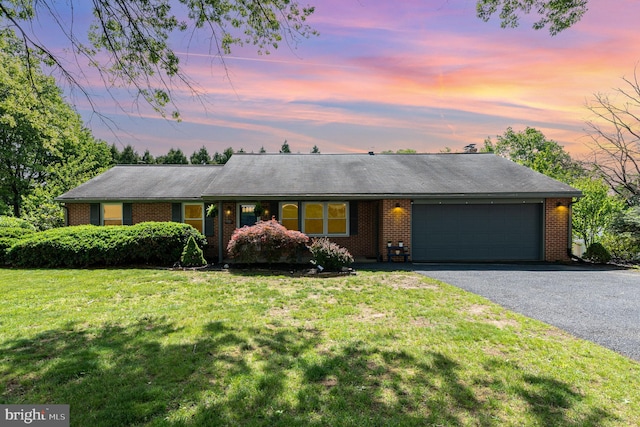 ranch-style house featuring a garage, asphalt driveway, a lawn, and brick siding