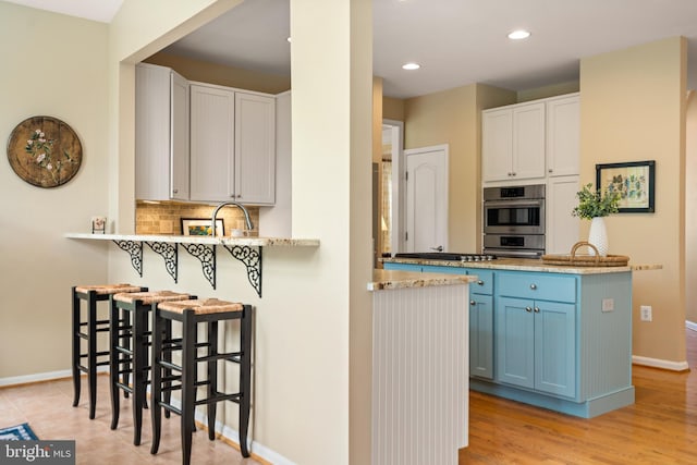 21381 Chickacoan Trail Dr, Broadlands, VA 20148 - kitchen with blue cabinetry, baseboards, tasteful backsplash, a kitchen breakfast bar, and a peninsula