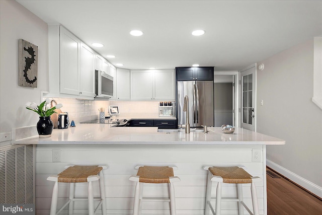 3 129th St Unit 7, Ocean City, MD 21842 - kitchen with stainless steel appliances, dark wood-type flooring, a peninsula, decorative backsplash, and white cabinetry