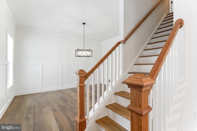 stairs with wood finished floors, a chandelier, a wainscoted wall, a decorative wall, and crown molding