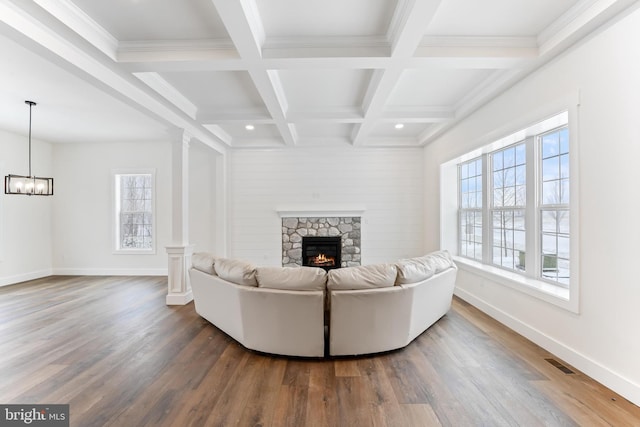 living room with a stone fireplace, wood finished floors, beam ceiling, decorative columns, and a chandelier