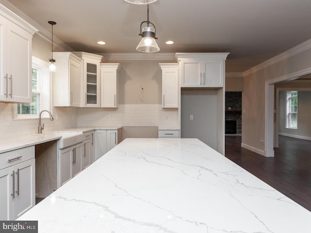 kitchen featuring a sink, ornamental molding, light stone counters, backsplash, and white cabinetry