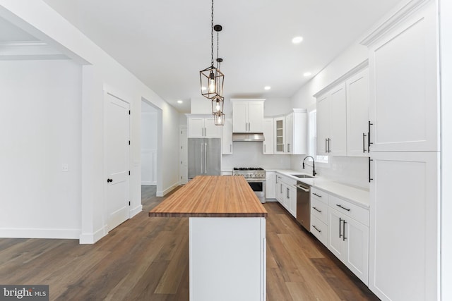 kitchen featuring butcher block countertops, premium appliances, recessed lighting, under cabinet range hood, and a sink
