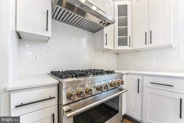kitchen with ventilation hood, stainless steel stove, white cabinetry, and tasteful backsplash