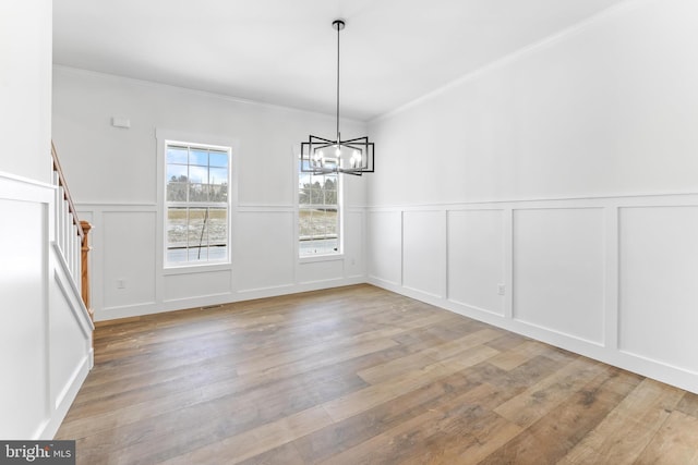 unfurnished dining area with a decorative wall, wood finished floors, wainscoting, a chandelier, and crown molding