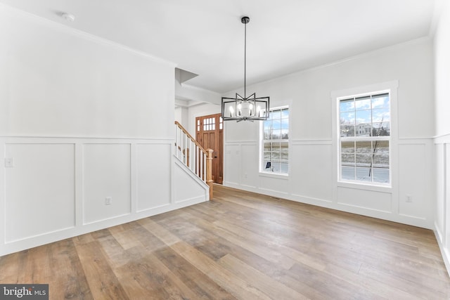 unfurnished dining area featuring a decorative wall, a chandelier, wainscoting, stairs, and wood finished floors