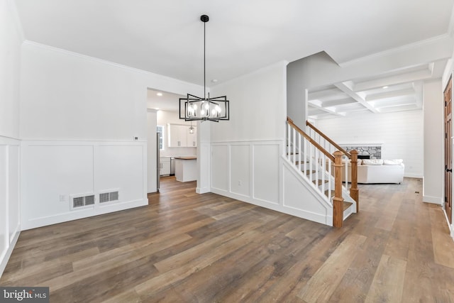 unfurnished dining area featuring a decorative wall, wood finished floors, a chandelier, stairs, and coffered ceiling