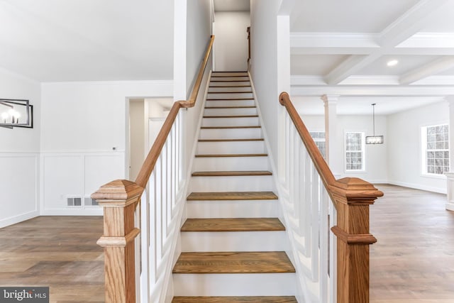staircase with ornamental molding, beam ceiling, wood finished floors, a wainscoted wall, and coffered ceiling