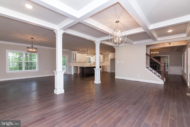 unfurnished living room featuring a chandelier, coffered ceiling, ornate columns, baseboards, and stairs