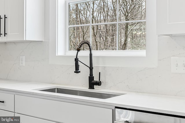 kitchen featuring tasteful backsplash, a sink, white cabinetry, light countertops, and dishwashing machine