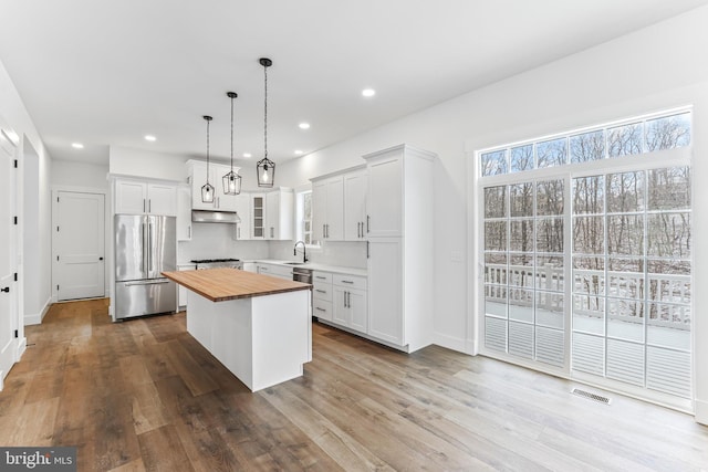 kitchen with freestanding refrigerator, butcher block countertops, under cabinet range hood, a kitchen island, and wood finished floors