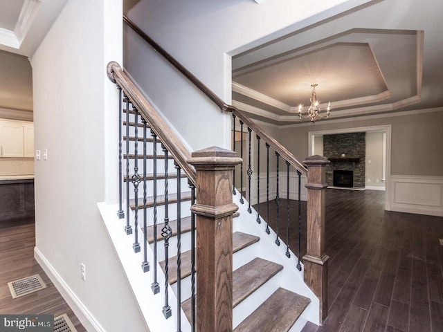 stairs featuring a tray ceiling, a chandelier, wood finished floors, crown molding, and wainscoting